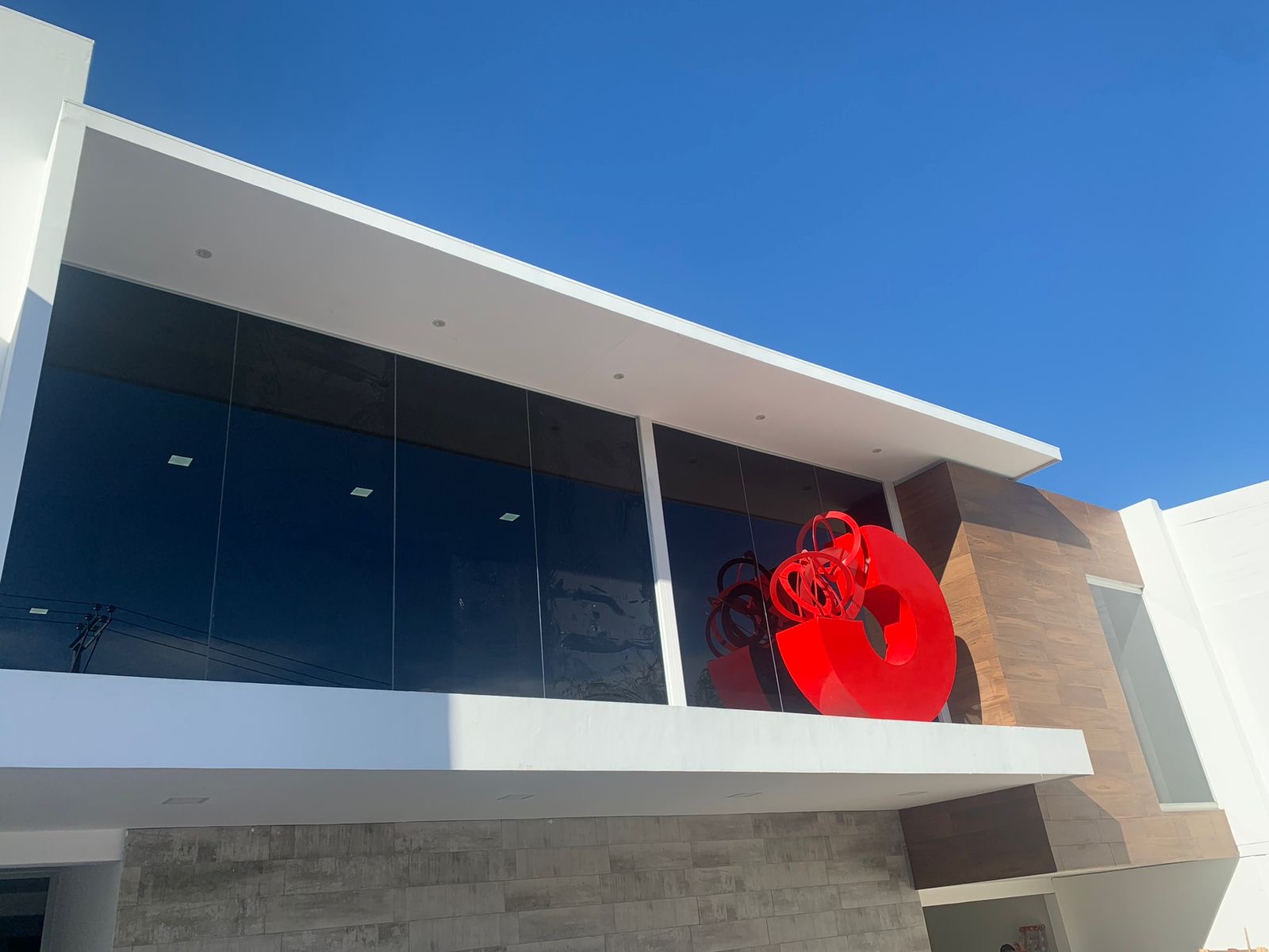 Edificio comercial con película nanocerámica de control solar SmartFilm en San Salvador, vidrio oscuro y escultura roja